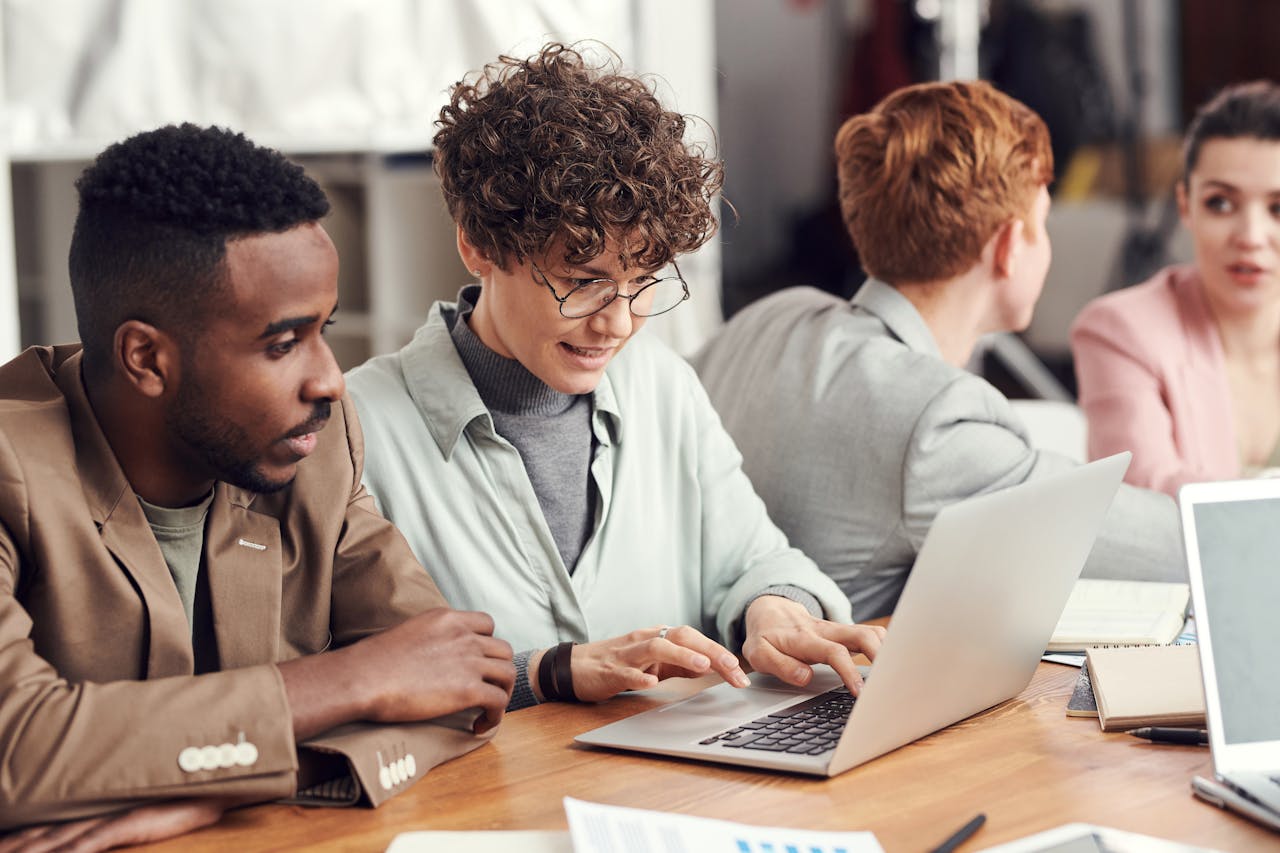 A group of diverse professionals engaged in a team meeting, working on laptops in a modern office setting.